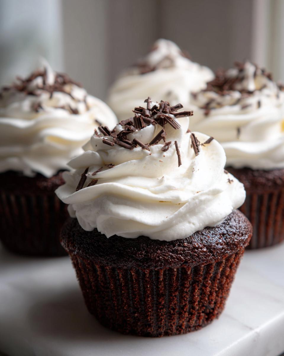 Close-up of decadent hot chocolate cupcakes topped with white whipped frosting and dark chocolate shavings.