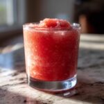 A close-up of a vibrant, icy strawberry daiquiri served in a clear glass on a granite countertop.