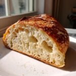 Close-up of a thick slice of homemade Italian bread showing a beautifully open, airy crumb and golden-brown crust.