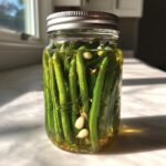 A glass jar filled with bright green, crunchy dilly beans, garlic cloves, and dill fronds submerged in pickling liquid.