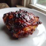 Close-up of a perfectly cooked, juicy piece of bbq chicken with a dark, sticky glaze.