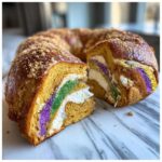 A slice cut from a rich, golden king cake showing layers of cream filling and vibrant purple, green, and gold edible glitter.
