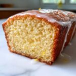 Close-up of a slice of moist lemon olive oil cake topped with a thick white glaze.