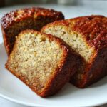 Close-up of moist, sliced banana bread showing the speckled texture and caramelized crust on a white plate.