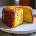 A slice cut from a moist orange juice cake, drizzled with a thick, shiny orange glaze.