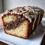 A close-up of a loaf of moist sour cream coffee cake featuring a cinnamon swirl center, topped with streusel and vanilla glaze.