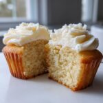Close-up of a vanilla cupcake cut in half showing the moist crumb texture and white vanilla frosting.