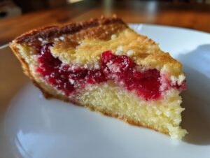Close-up of a moist slice of Nantucket cranberry pie showing the bright red cranberry filling and golden cake base.