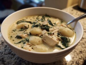 A close-up of a white bowl filled with creamy Olive Garden Chicken Gnocchi Soup, showing chunks of chicken, spinach, and soft gnocchi.