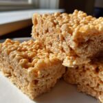 A stack of three thick, chewy peanut butter rice krispie treats showing the texture of the puffed rice cereal.