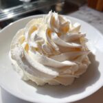 A beautiful, stiff swirl of white cream cheese frosting piped onto a small white plate, showing texture.
