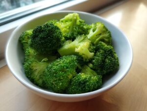 A close-up of vibrant green steamed broccoli florets served in a white bowl, ready to eat.