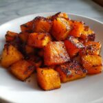 Close-up of beautifully caramelized and seasoned roasted butternut squash cubes piled on a white plate.