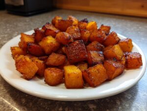 A mound of caramelized, perfectly roasted butternut squash cubes served on a white plate.