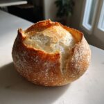 A freshly baked, round artisan bread bowl with a golden, cracked crust and visible airy interior.