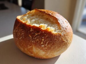 A close-up of a freshly baked, round bread bowl with a golden crust, ready to be filled with soup.