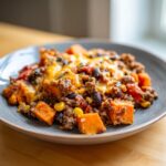 A close-up of a savory sweet potato skillet mixture with ground meat, black beans, corn, and melted cheese on a blue plate.