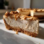Close-up of a thick slice of creamy biscoff cheesecake on a white plate, topped with Biscoff drizzle.