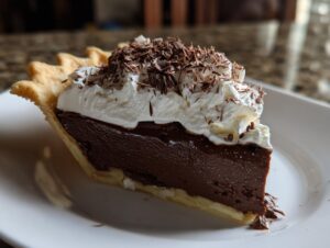 A decadent slice of french silk pie featuring a thick chocolate filling, topped with whipped cream and chocolate shavings.
