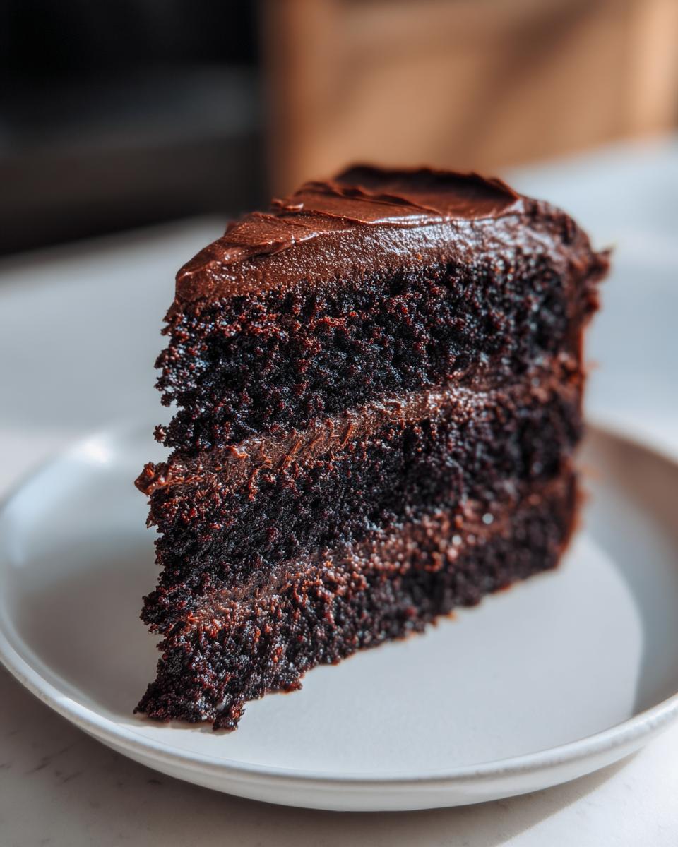 Close-up of a rich, dark slice of homemade chocolate cake layered with thick chocolate frosting.