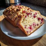 A loaf of cranberry walnut bread, sliced to show the moist interior packed with cranberries and topped with walnuts.