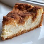 Close-up of a creamy slice of snickerdoodle cheesecake with a thick cinnamon-sugar topping and graham cracker crust.