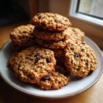 A tempting stack of soft oatmeal cookies loaded with raisins, presented on a light-colored plate.
