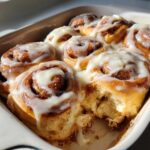 Close-up of gooey sourdough discard cinnamon rolls baked together in a dish, generously topped with white cream cheese icing.