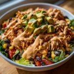 A vibrant bowl of southwest chicken salad topped with shredded seasoned chicken, avocado, and creamy dressing.