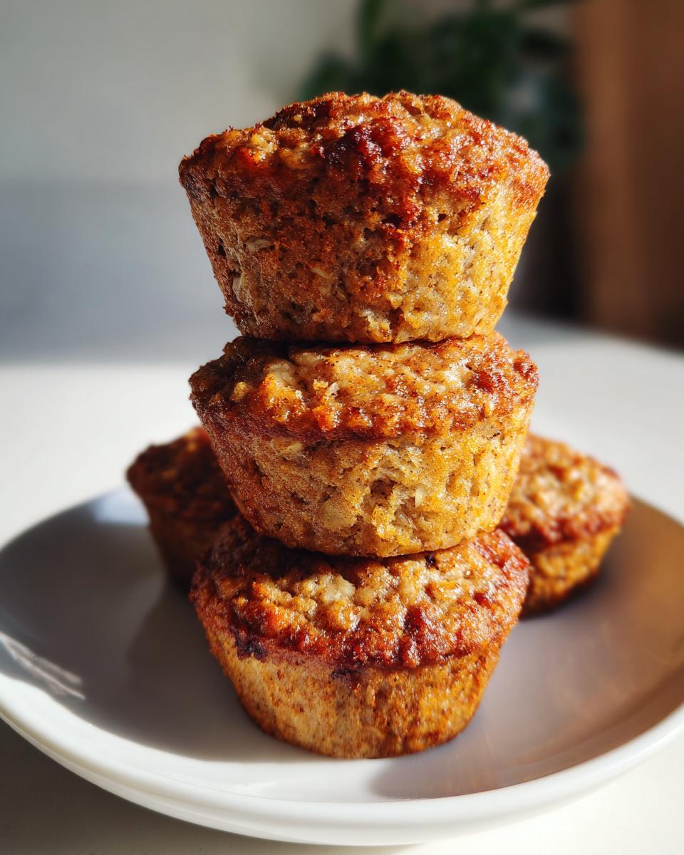 A stack of three golden-brown, healthy oatmeal muffins sitting on a white plate, highlighted by bright sunlight.