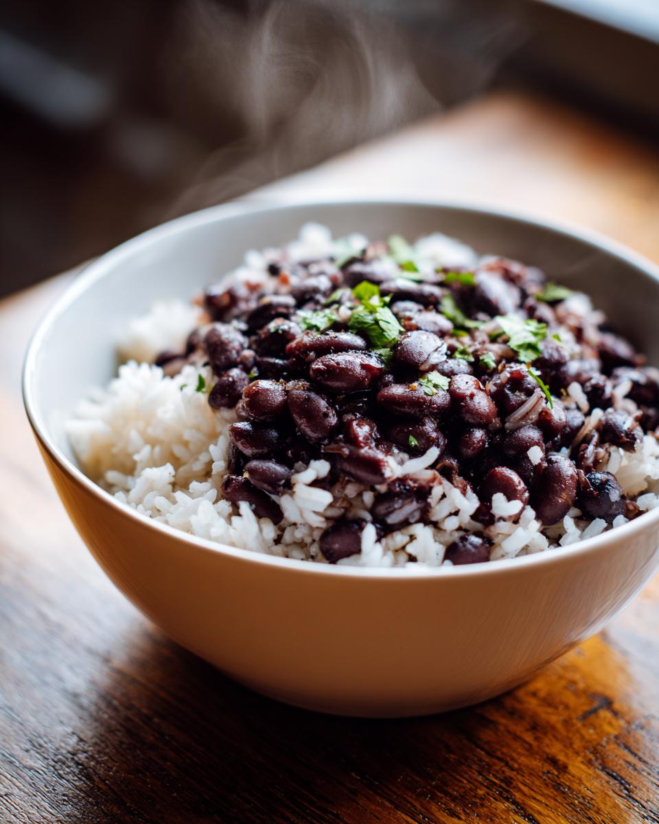 Close-up of a steaming white bowl filled with white rice topped generously with seasoned black beans and fresh cilantro, perfect for beans and rice dinner.