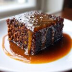 Close-up of a rich, dark slice of sticky toffee pudding recipe drenched in warm toffee sauce.