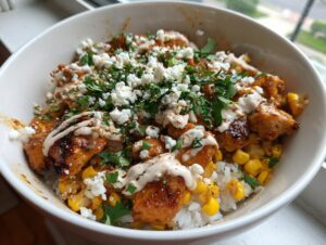 A close-up of a vibrant street corn chicken rice bowl topped with cotija cheese, cilantro, and a creamy drizzle.