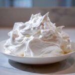 A white bowl filled with stiff, glossy peaks of sugar cookie icing that hardens, ready for decorating.