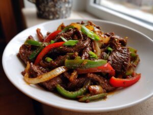 Close-up of tender beef pepper steak stir-fry with vibrant red and green bell peppers and onions.