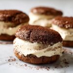 A close-up of one perfectly assembled tiramisu cookies sandwich filled with creamy mascarpone, dusted heavily with cocoa powder.