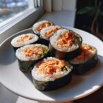 A plate of freshly cut tuna kimbap rolls showing the orange tuna filling and rice wrapped in nori seaweed.