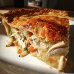 Close-up of a slice of turkey pot pie recipe showing shredded turkey, carrots, and creamy filling under a golden, flaky crust.