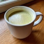 A close-up of velvety celery soup with a light green hue served hot in a white mug.