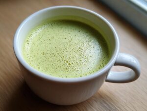 Close-up of a white mug filled with velvety, light green celery soup, showing a frothy top.