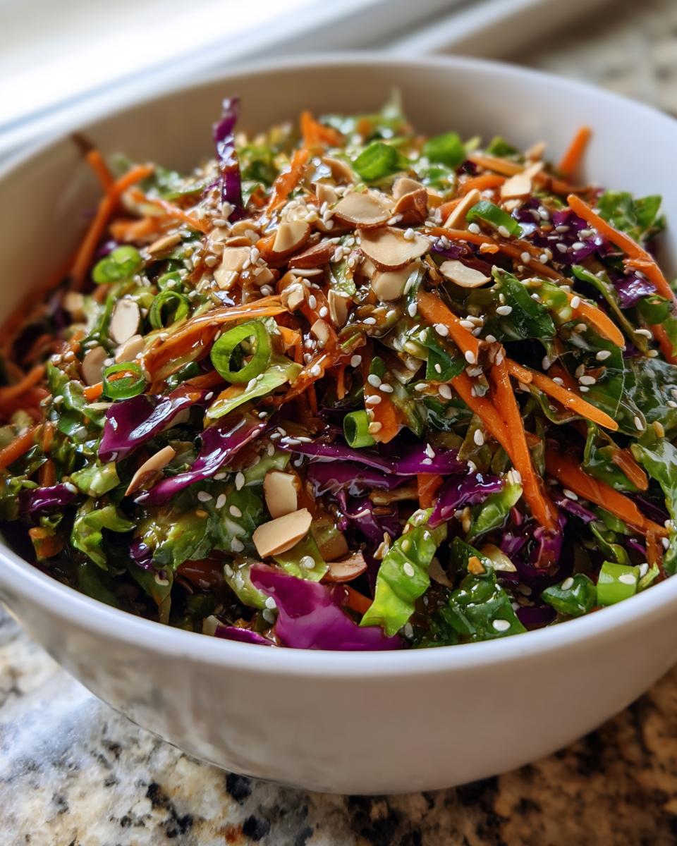 Close-up of a vibrant cabbage salad featuring shredded red and green cabbage, carrots, and a savory dressing, topped with sliced almonds and sesame seeds.