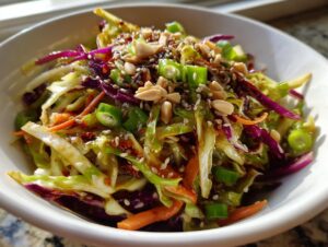 Close-up of a vibrant cabbage salad featuring shredded green and purple cabbage, carrots, green onions, and topped with peanuts and sesame seeds.