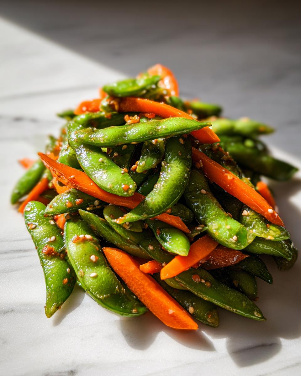 Close-up of a vibrant edamame salad featuring bright green edamame pods mixed with sliced carrots and sprinkled with sesame seeds.