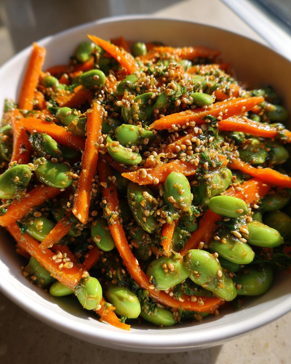 Close-up of a vibrant edamame salad featuring bright green edamame beans, julienned carrots, and a sesame seed dressing.