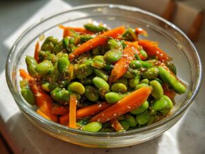 Close-up of a vibrant edamame salad with bright orange carrot strips, tossed in a light dressing and sprinkled with sesame seeds.