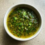 Overhead view of a small white bowl filled with chunky, bright green tomato salsa, topped with fresh cilantro.