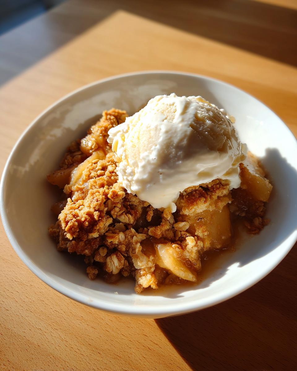A warm serving of apple crumble topped with a melting scoop of vanilla ice cream, perfect for this comfort recipe.