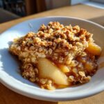 A close-up of a warm serving of pear crisp with a thick, crunchy oat topping and soft, caramelized pears.