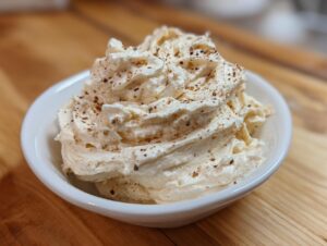A close-up of fluffy, whipped cinnamon butter sprinkled with ground cinnamon in a small white bowl.