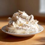 A mound of fluffy whipped cream, likely flavored with cinnamon butter, dusted with cinnamon on a small white plate.